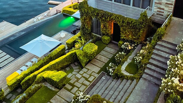 A modern building with a pool, surrounded by well-manicured gardens and a view of the water.