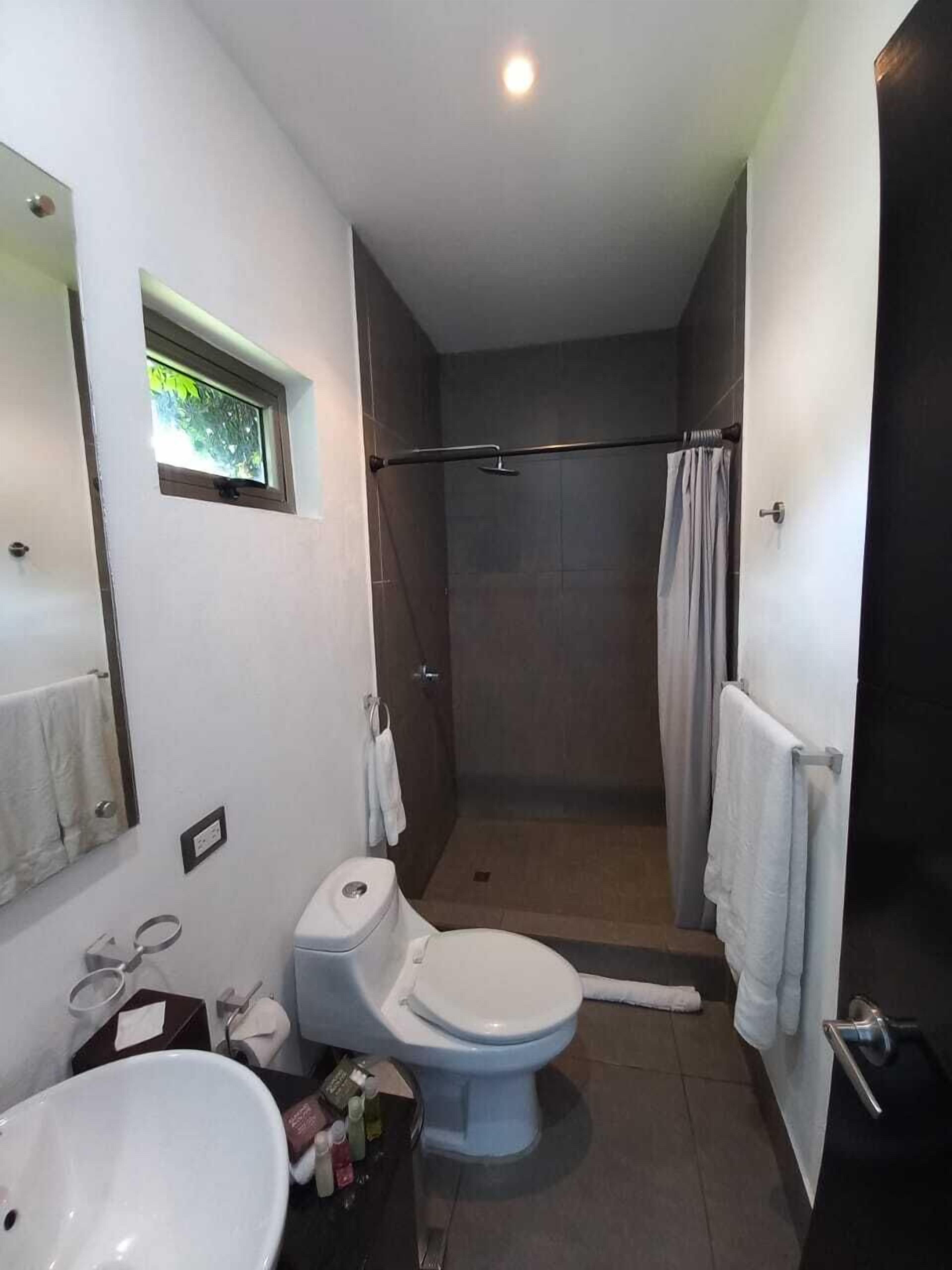 A bathroom with a toilet, sink, shower, and a small window.