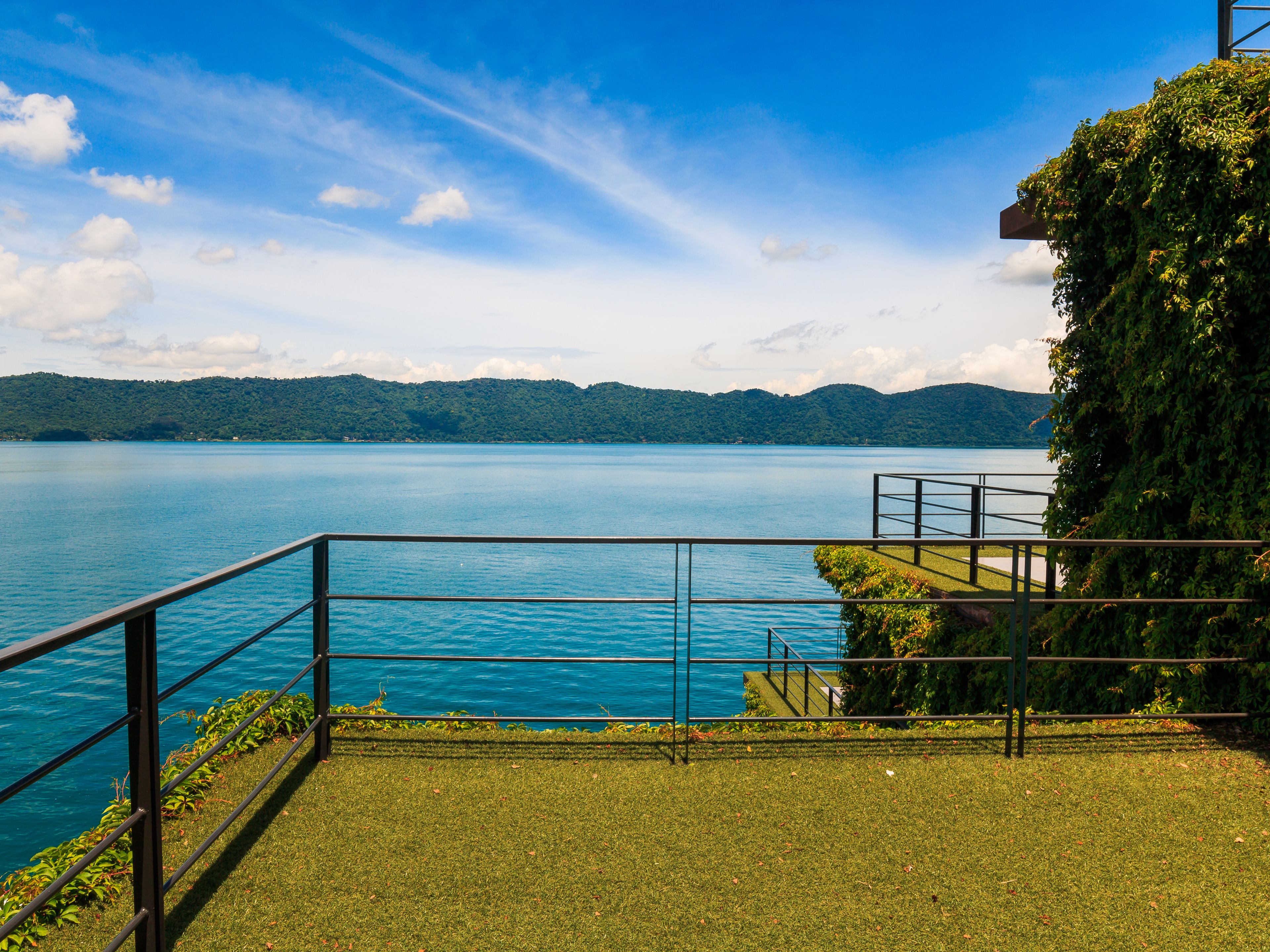 A lakeside view with a grassy area, metal railing, and a stone pathway leading to a dock.