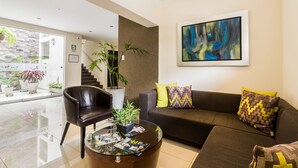 A modern living room with a glass coffee table, a black leather chair, a brown sofa with patterned cushions, and a large abstract painting on the wall. - Tambo Dos de Mayo (Lima)