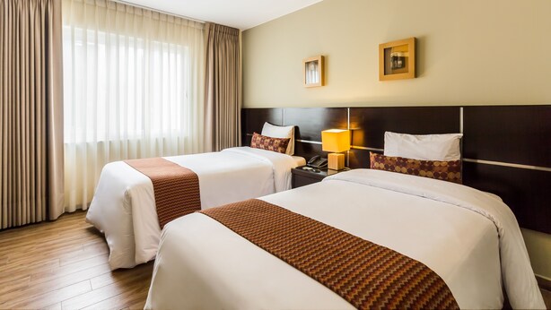 A hotel room with two beds, a wooden floor, a large window with curtains, and a wall-mounted lamp. - Tambo Dos de Mayo (Lima)