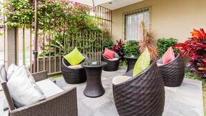 An outdoor patio area with wicker furniture, a glass table, and various potted plants. - Tambo Dos de Mayo (Lima)