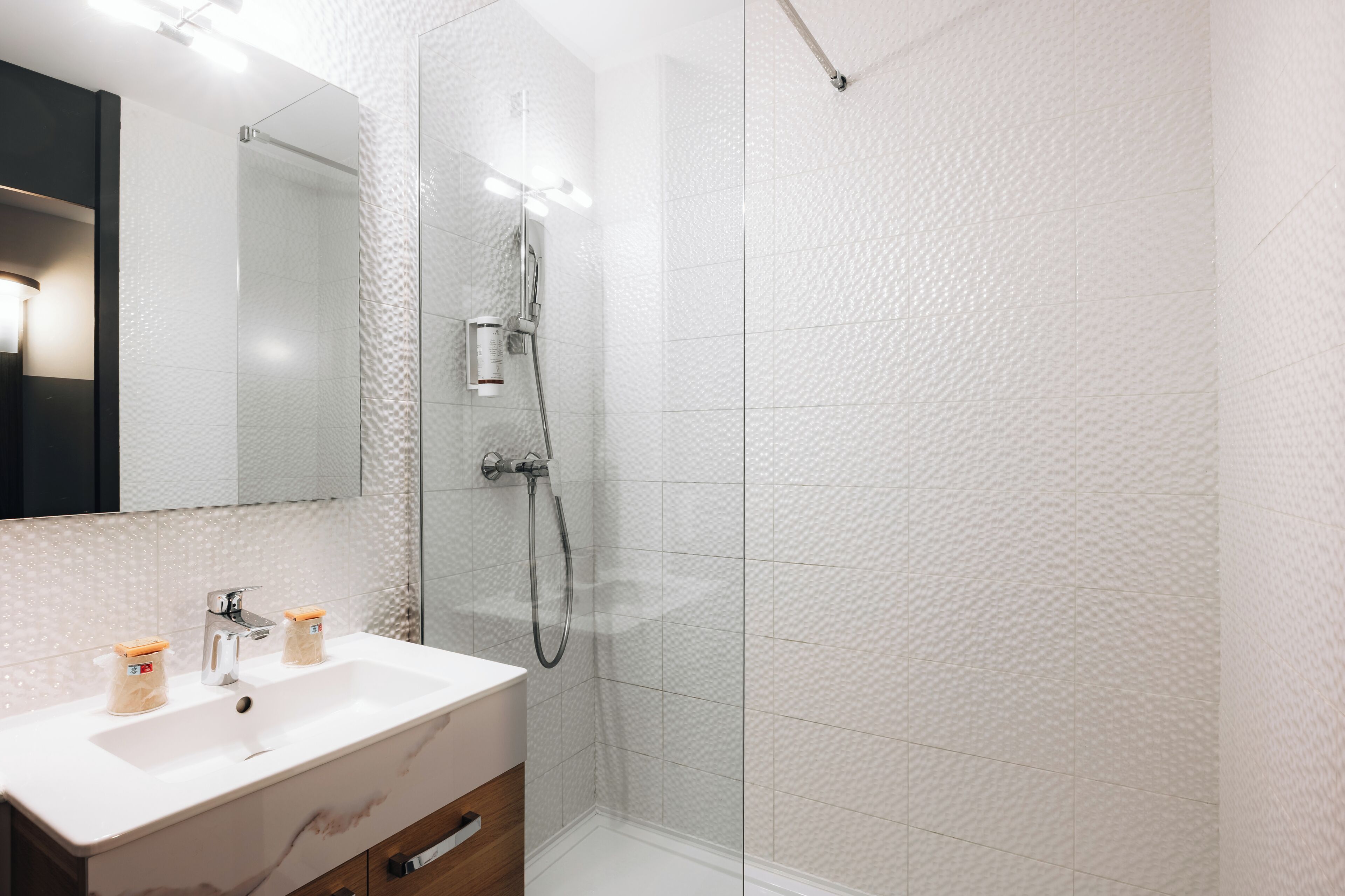 A modern bathroom with a glass-enclosed shower, a white sink with a marble countertop, and a wooden cabinet below.