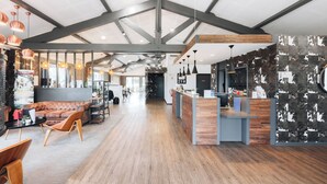 A spacious interior with a high ceiling, exposed beams, and a mix of seating areas including a sofa and a table with chairs. - Best Western Portes d’Aquitaine Agen Sud (Le Passage)