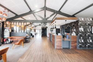 Un interior amplio con techo alto, vigas a la vista y una variedad de espacios de descanso, incluyendo un sofá y una mesa con sillas.