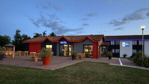Een hotel met een gevel in rood en grijs, een bord met daarop 'HOTEL' en een verzorgd terras met stoelen en tafels.