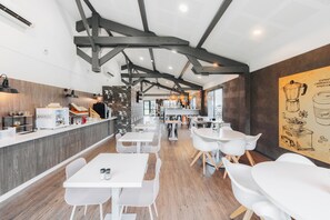A modern café interior with exposed beams, white tables, and a mural on the wall. - Best Western Portes d’Aquitaine Agen Sud (Le Passage)