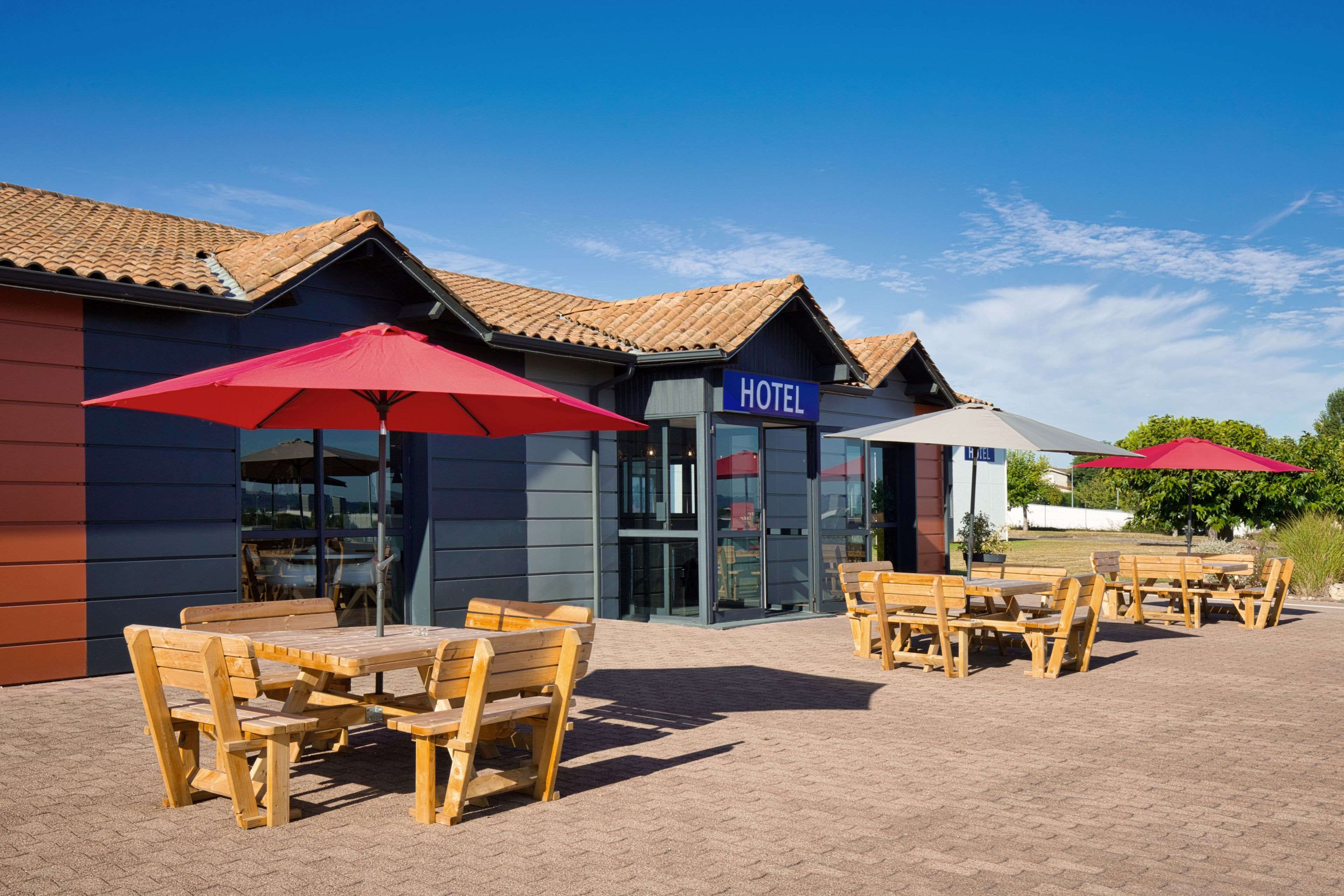 A hotel with outdoor seating and red umbrellas.