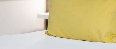 Una cama con colchón blanco, almohada amarilla y cabecera de madera.