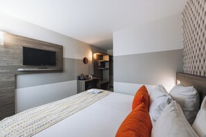Habitación de hotel con cama, televisor de pantalla plana en la pared, escritorio con silla y microondas.