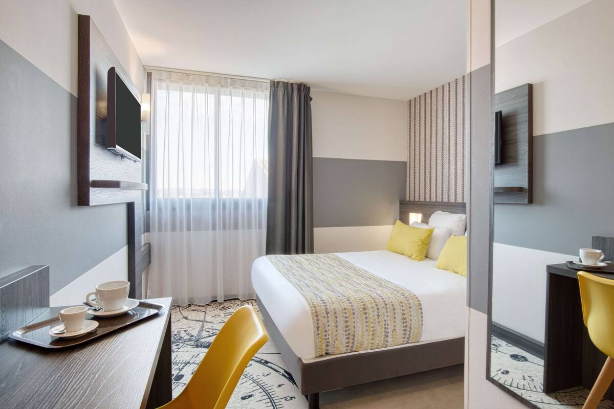 Ein Hotelzimmer mit einem Bett, einem Schreibtisch mit einer Kaffeetasse und einem Stuhl sowie einem großen Spiegel.