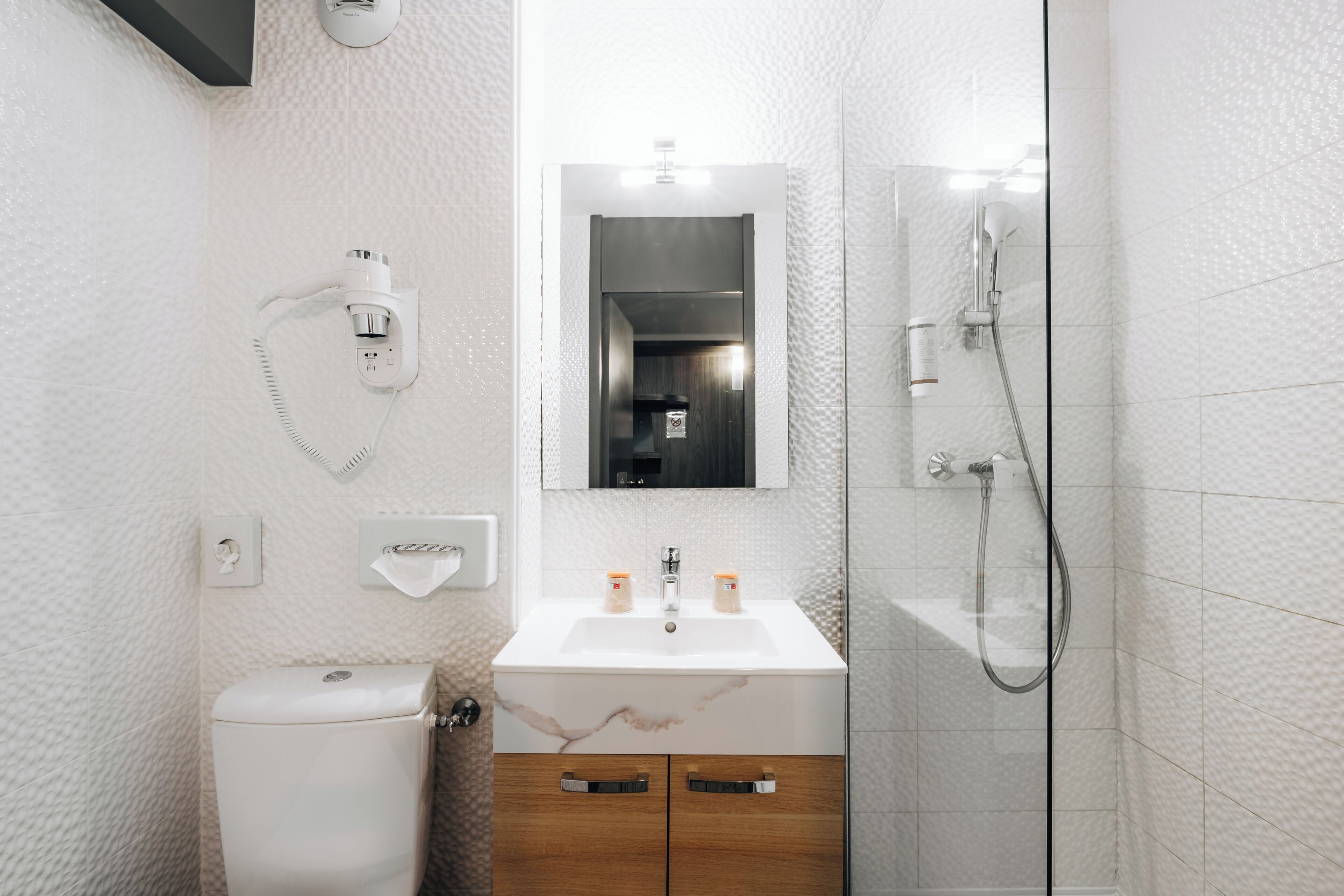 Un baño moderno con inodoro, lavamanos, espejo y ducha.
