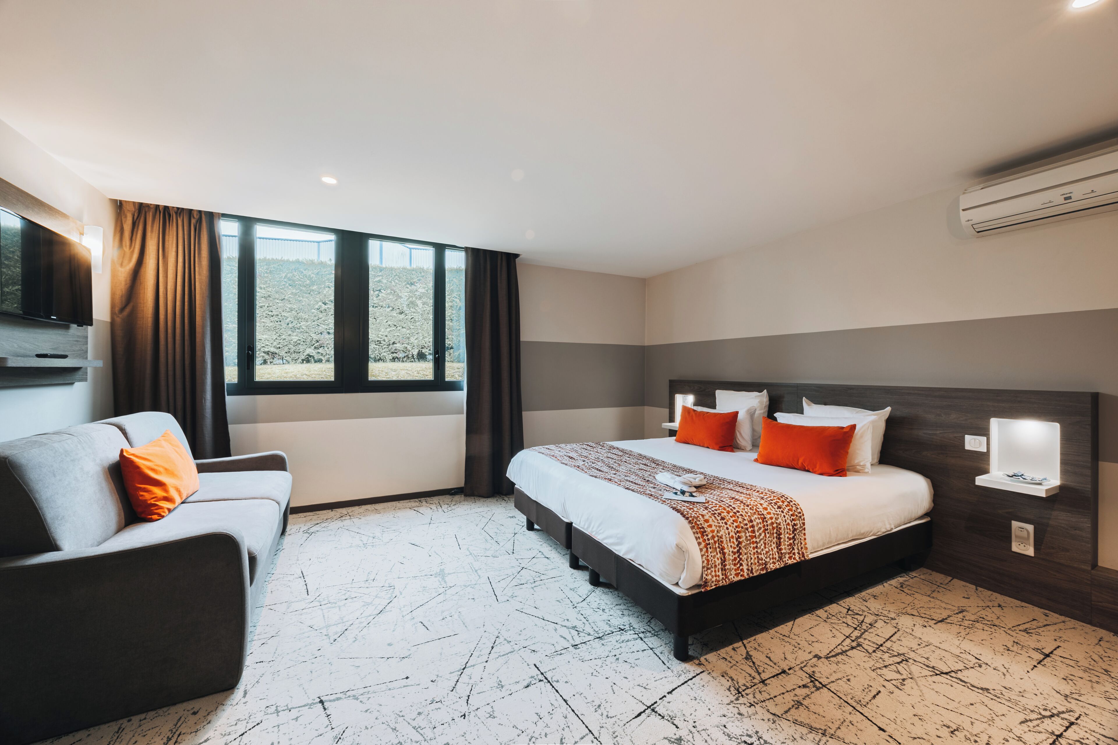 Een hotelkamer met een bed, een sofa, een televisie en een raam met gordijnen.