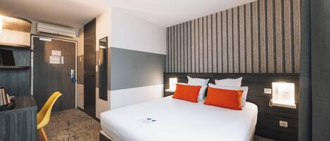 A hotel room with a bed, bedside tables, a desk, a chair, and a wall-mounted light fixture.