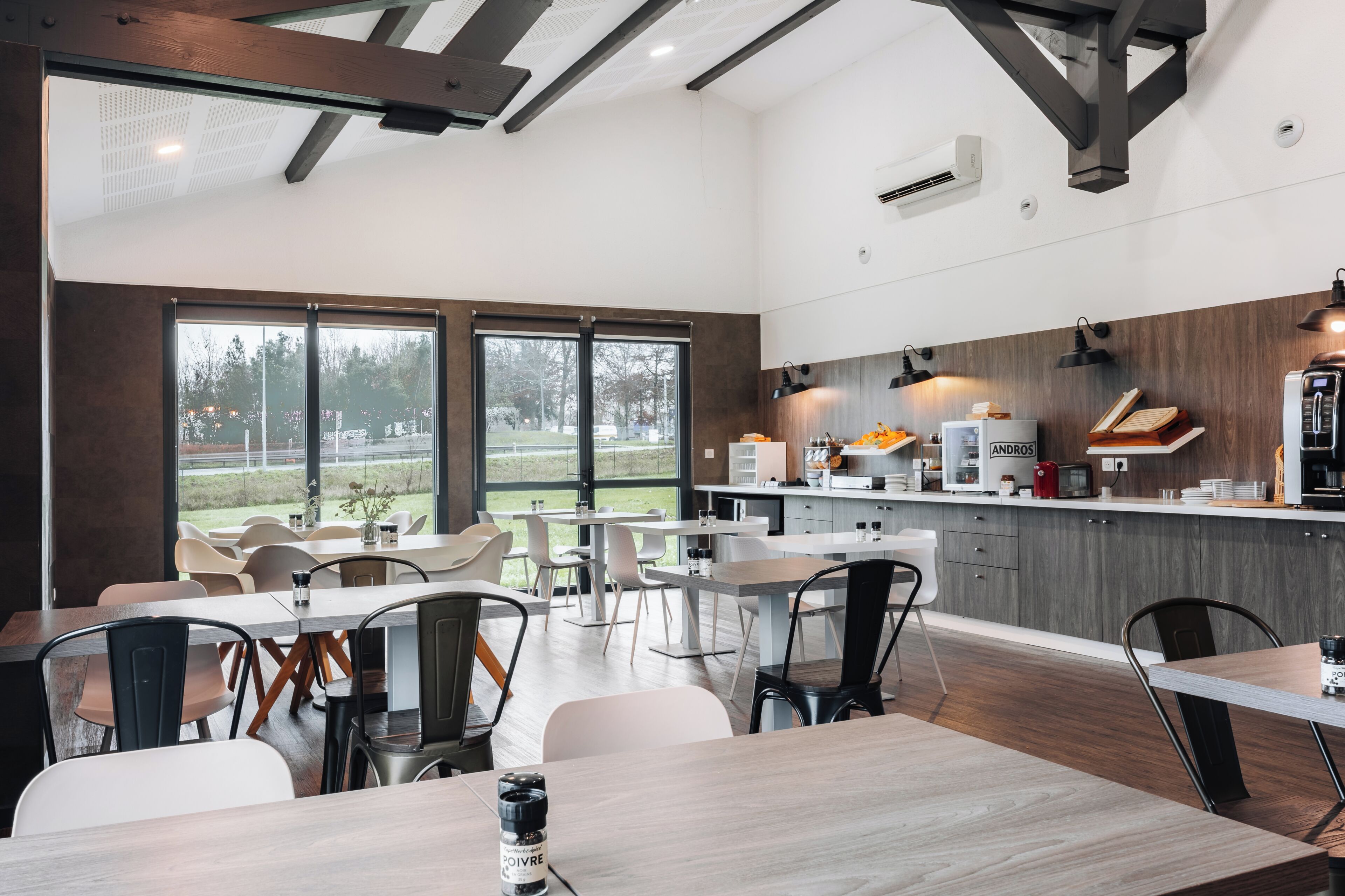 Een moderne eetruimte met tafels en stoelen, een keuken met inbouwapparatuur, en grote ramen met uitzicht op de omgeving.