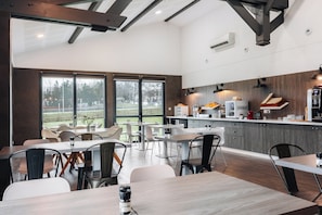 Een moderne eetruimte met tafels en stoelen, een keuken met inbouwapparatuur, en grote ramen met uitzicht op de omgeving.