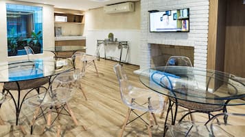 A modern meeting room with glass tables and chairs, a white brick fireplace, and a mounted TV.