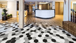 A hotel lobby with a central reception desk, wooden flooring, and hexagonal patterned tiles. - H Hotel (Balneário Camboriú)