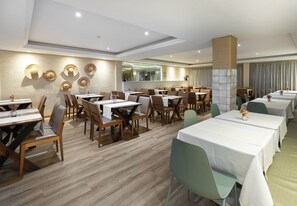 Un comedor de hotel con varias mesas y sillas, un espejo grande y una pared decorativa con sombreros.