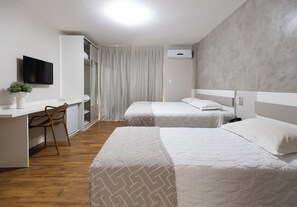 Habitación de hotel con escritorio, dos camas, televisor y una planta.