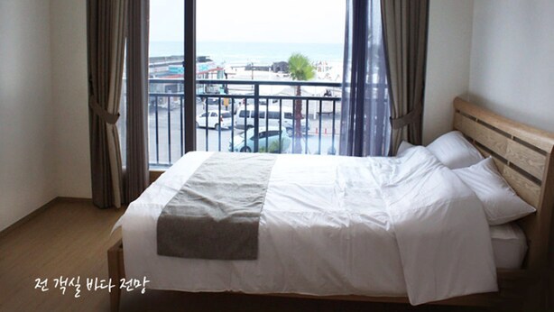 A hotel room with a large bed, a view of the sea and a balcony. - Gilgaon Pension (Jeju City)