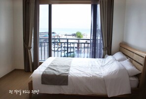 A hotel room with a large bed, a view of the sea and a balcony. - Gilgaon Pension (Jeju City)