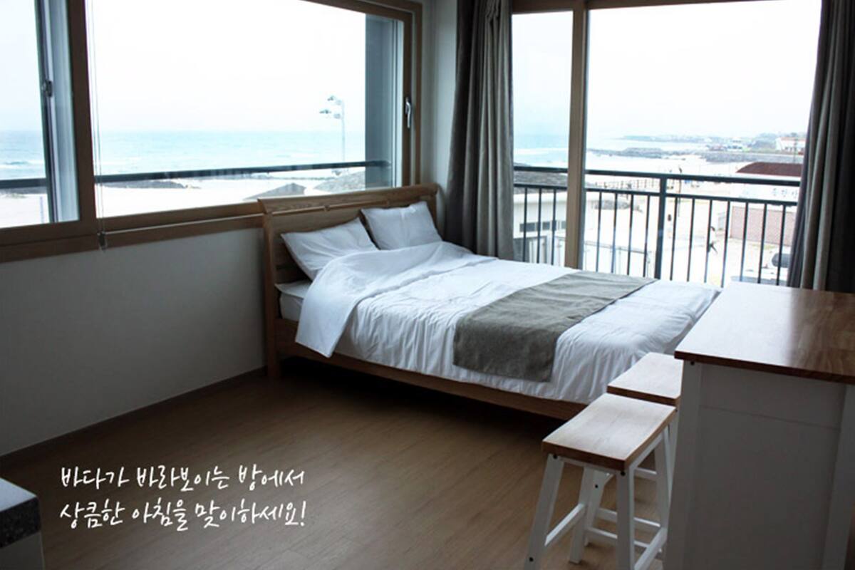 A bedroom with a bed, a desk, and a view of the sea.