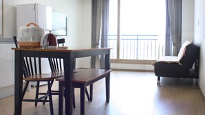 A hotel room with a dining table, chairs, a sofa, a TV, and a balcony with curtains. - Gilgaon Pension (Jeju City)