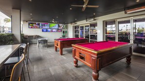 Un espace dédié au billard, comprenant deux tables de billard, des chaises et un coin bar avec un écran de télévision.