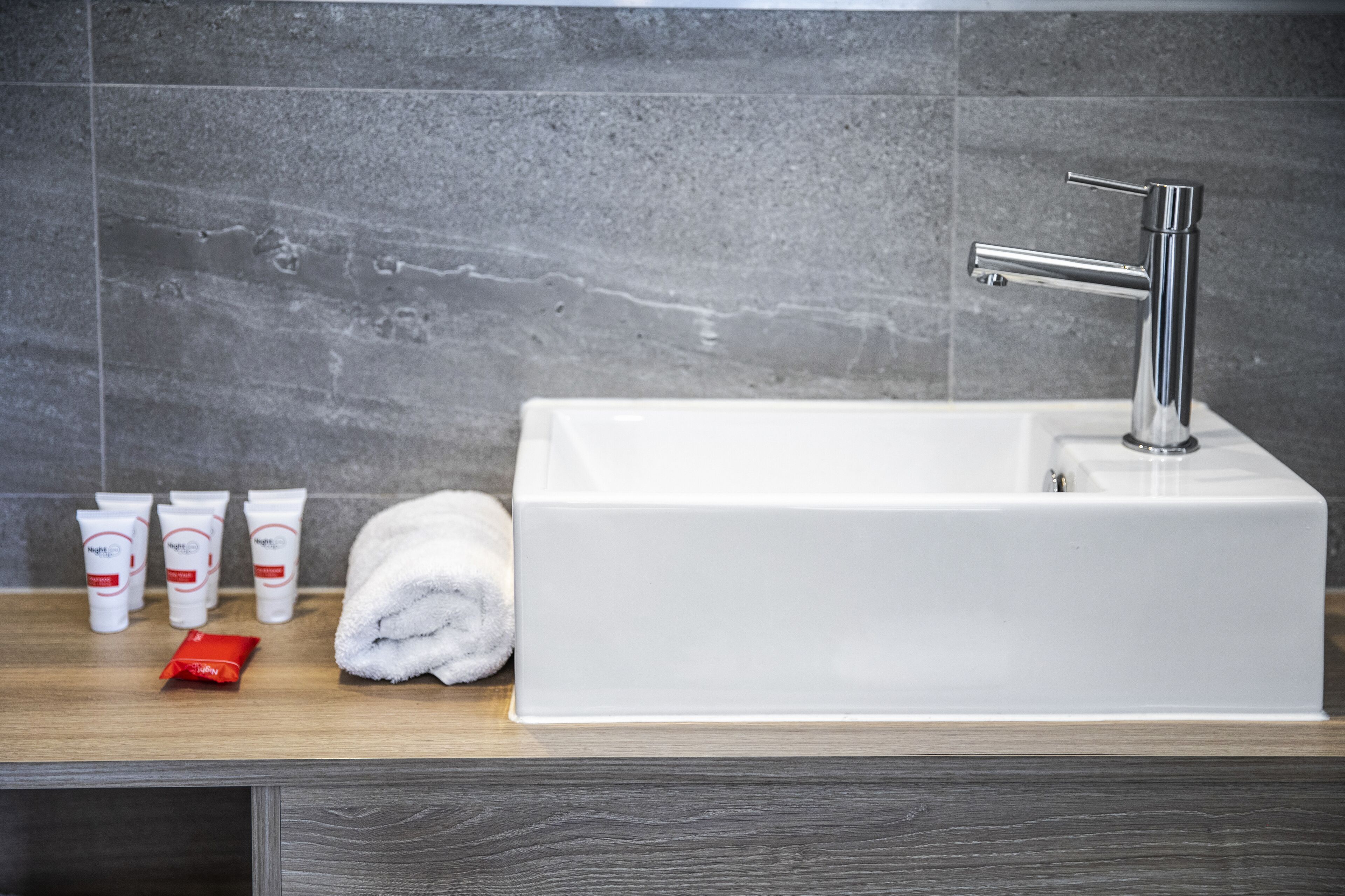 A bathroom with a white sink, a towel, and toiletries on a wooden countertop.