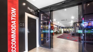 L’entrée d’un hôtel, avec une porte en verre, un comptoir d’accueil et un panneau indiquant la zone réservée aux chambres.
