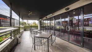 Un espace extérieur aménagé en terrasse, avec des tables et des chaises, une poubelle et un panneau indiquant les offres de l’hôtel.