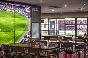 A sports bar with multiple viewing screens displaying a soccer match, tables numbered for seating, and a large window with a view of the field. - Nightcap at Ashley Hotel (Braybrook)
