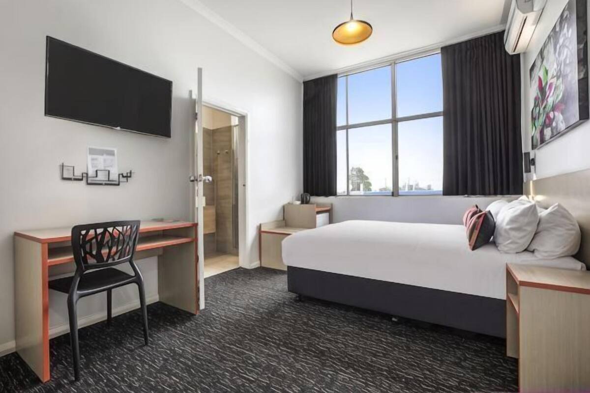 A hotel room with a bed, desk, chair, TV, and a window with a view.