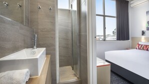 Une chambre d’hôtel moderne dotée d’un grand lit, d’une douche séparée avec des portes en verre, d’une baignoire et d’une fenêtre avec des rideaux.