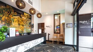 A hotel reception area with a marble counter, a large wall mural, and a patterned carpet. - Nightcap at Millers Inn (Altona North)