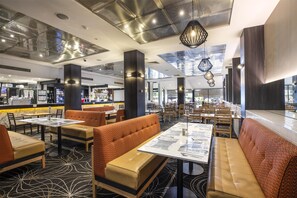 Un restaurante moderno con techos altos, amplias ventanas y diversas opciones de asientos, incluyendo cabinas y mesas.