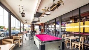 A billiards table in a restaurant with large windows and indoor seating. - Nightcap at Millers Inn (Altona North)