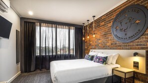 A hotel room with a large bed, a nightcap hotel sign, a TV, and a brick wall. - Nightcap at Millers Inn (Altona North)