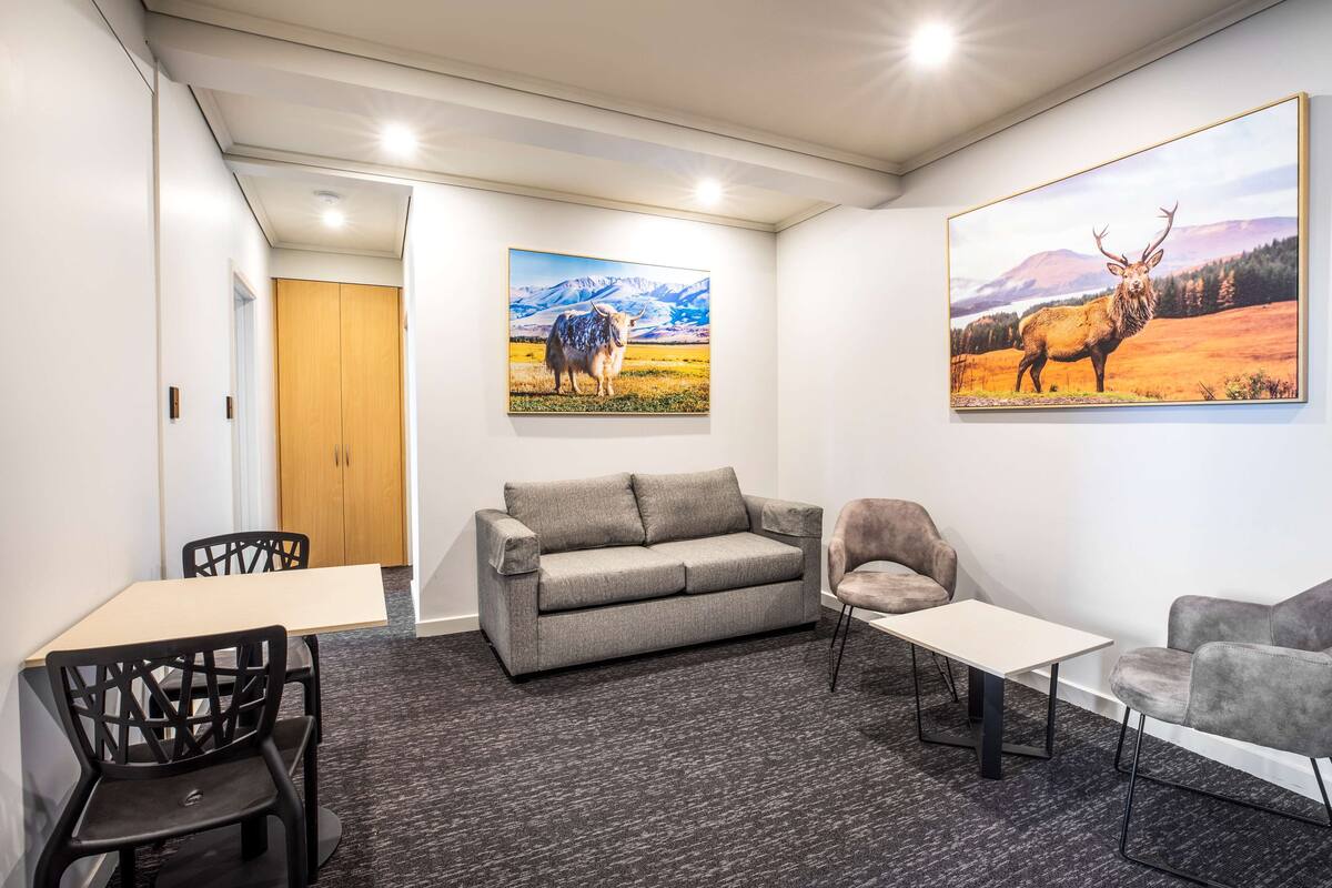 Ein modernes Zimmer mit einem grauen Sofa, zwei Sesseln, einem kleinen Tisch und zwei Wildtierbildern.