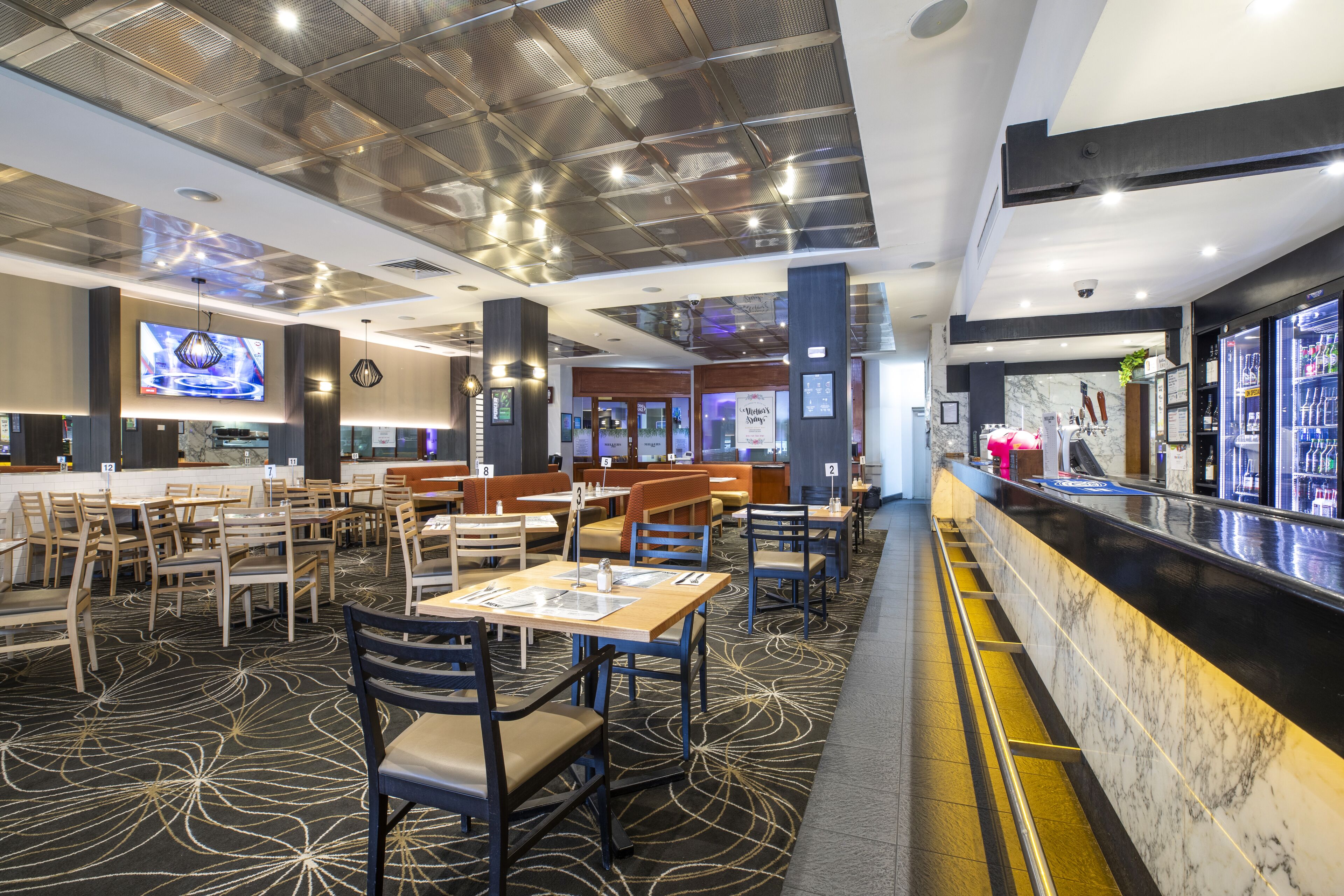 A modern restaurant with a marble counter, multiple seating areas, and a large screen displaying content.