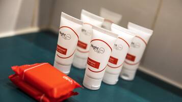 Une rangée de produits de toilette d’hôtel blancs, avec des inscriptions rouges et noires sur une surface turquoise.