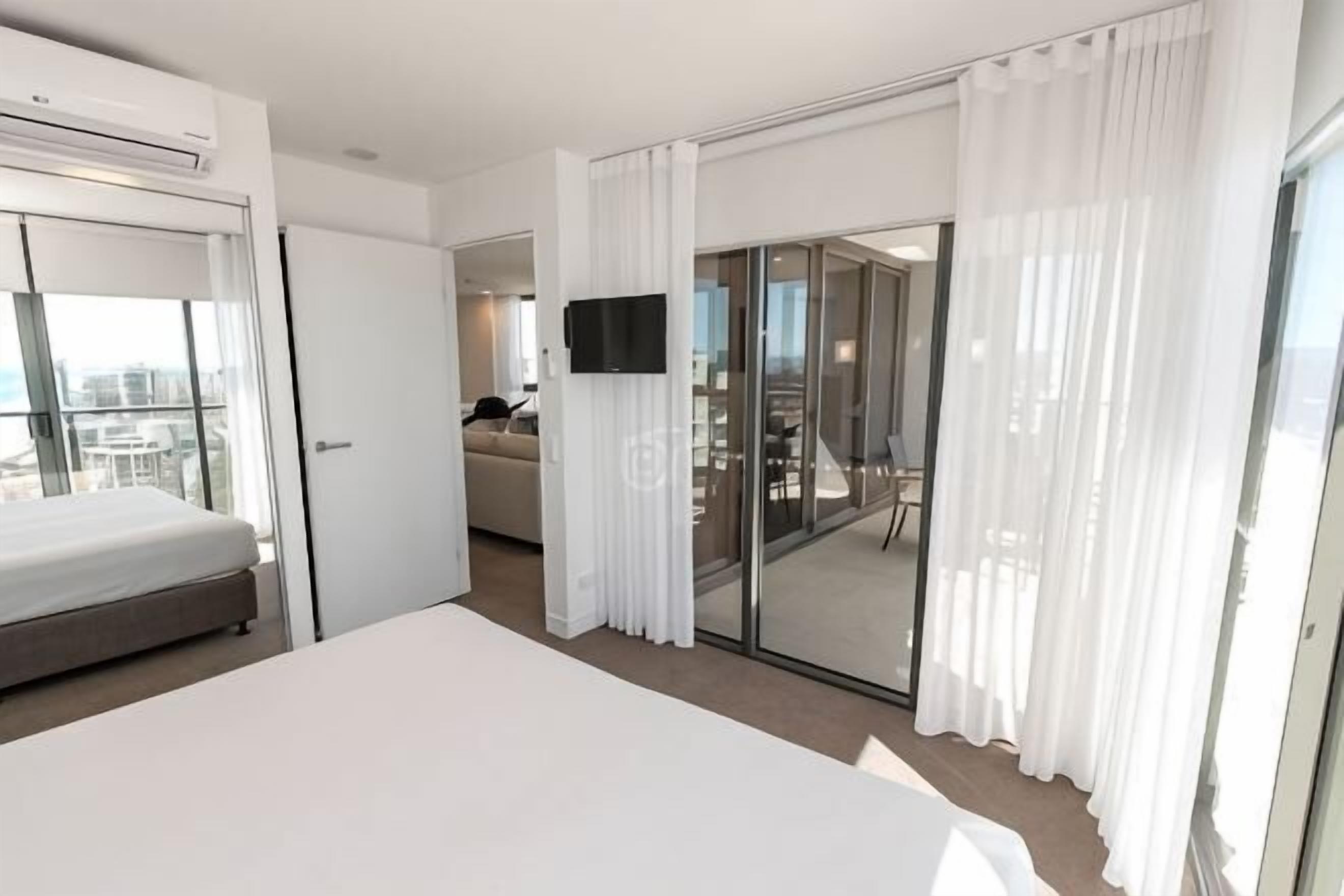 Hotelkamer met een bed, een televisie, een schuifglasdeur naar een balkon en uitzicht op de stad.