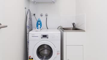 Un lavadero pequeño con lavadora de carga frontal, un lavabo y un perchero.
