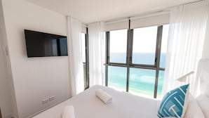 Une chambre d’hôtel dotée d’un grand lit, d’un téléviseur à écran plat fixé au mur et offrant une vue sur l’océan grâce à de grandes fenêtres.