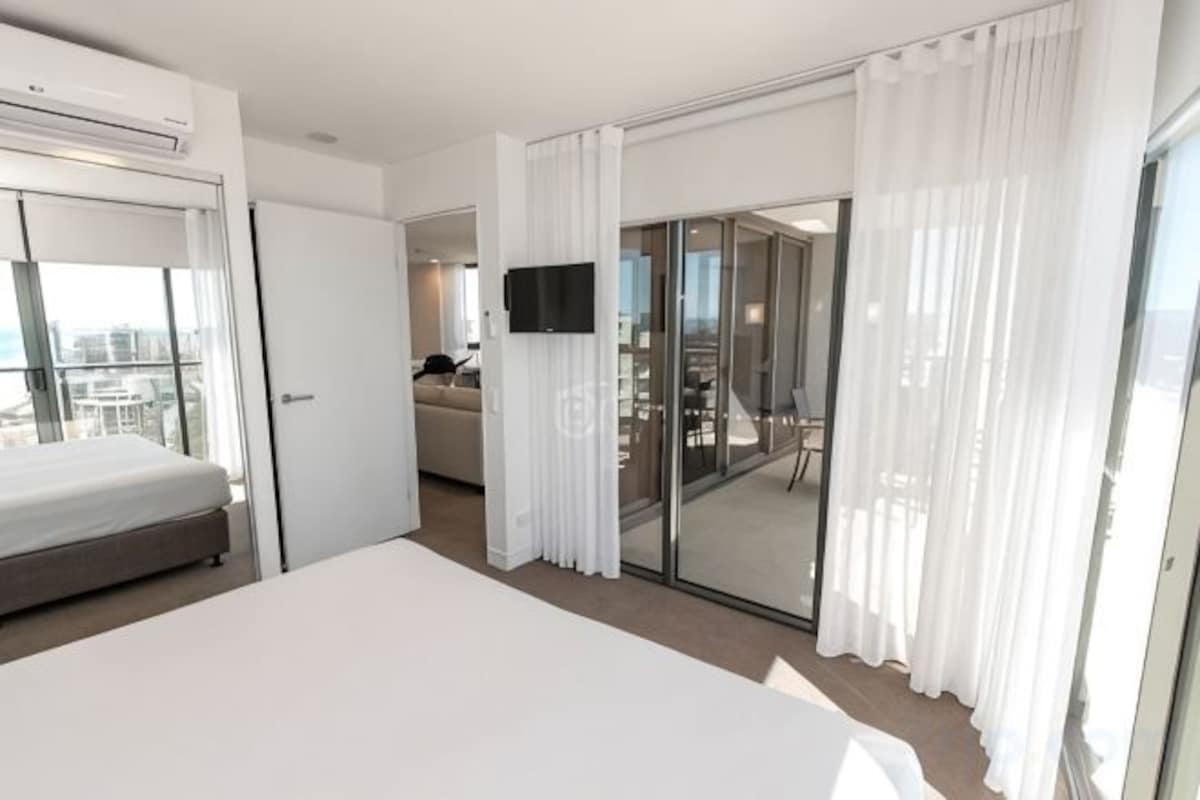 Een hotelkamer met een bed, een televisie, een schuifglazen deur naar een balkon en uitzicht op de stad.