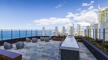 Terraza en la azotea con asientos, un bar y vistas al horizonte de la ciudad y al agua.