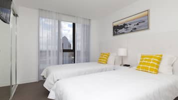 A hotel room with two beds, a window with curtains, a painting on the wall, and a nightstand with a lamp.