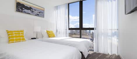 A hotel room with two beds, a large window with curtains, a painting on the wall, and a flat-screen TV.