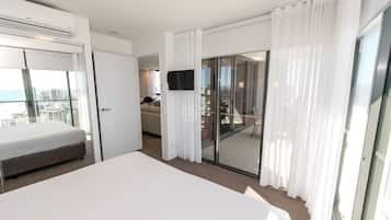 A modern hotel room with a large bed, a TV, a balcony with a city view, and a sliding glass door.
